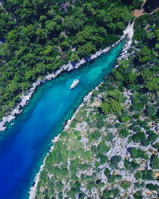 Buzağılık Cove straight down: a narrow turquoise channel between pine-covered rock, a single boat in it