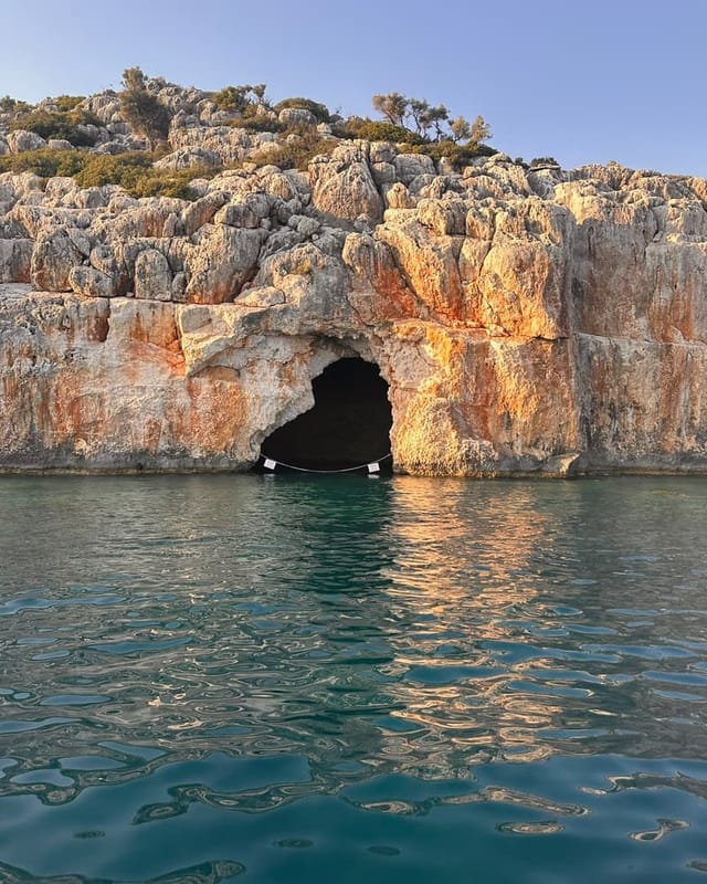 The Pirate Cave: a dark mouth in limestone turned orange by the low sun, the water still